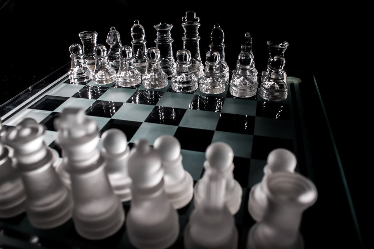 Close-up of frosted and clear glass chess pieces on a chessboard, symbolizing strategy and intelligence.